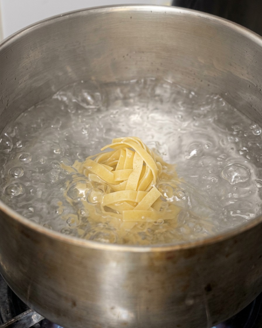 Breite Bandnudeln werden in einen Topf mit sprudelnd kochendem Wasser gegeben.