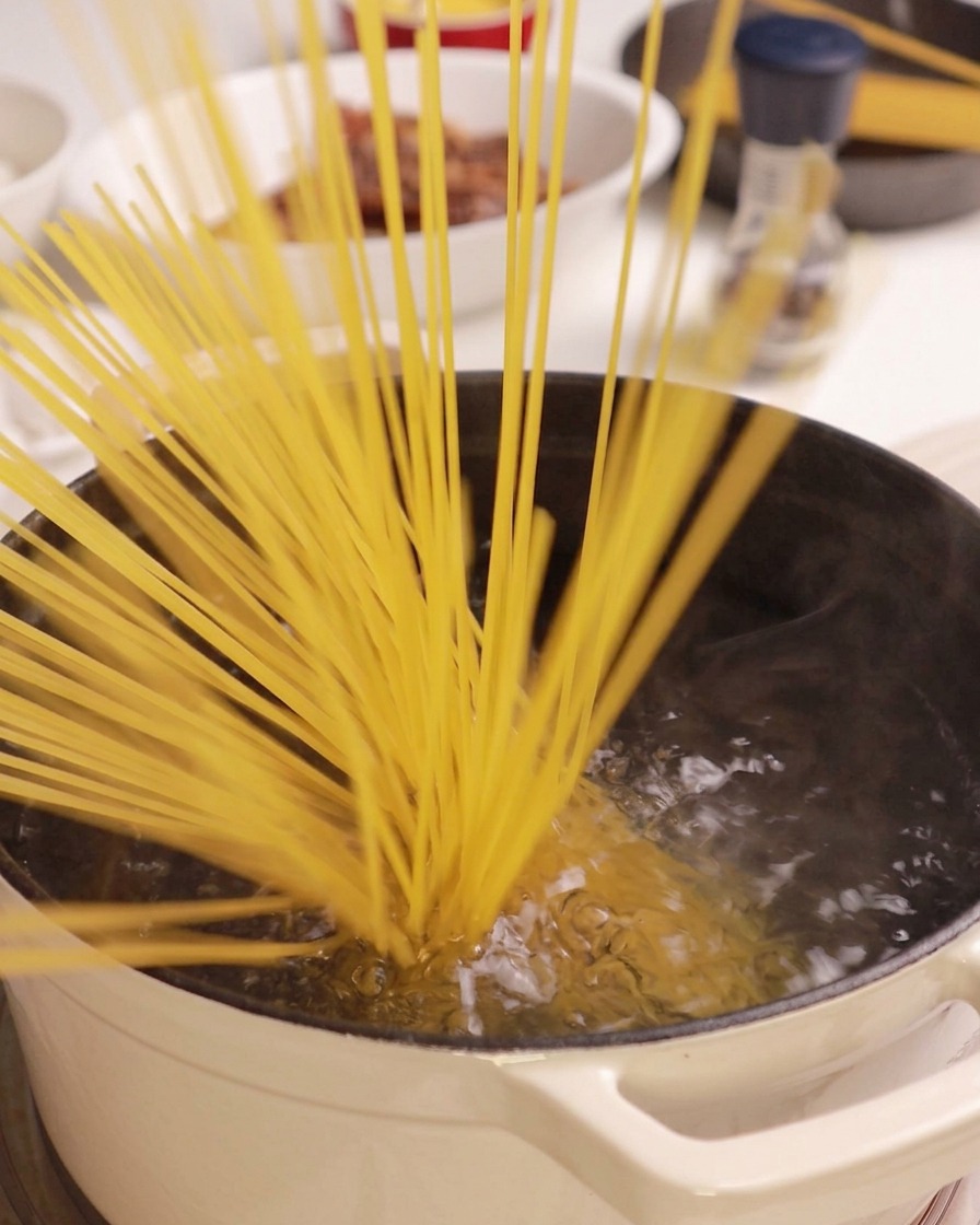 Ein Bündel trockener Spaghetti wird in einen Topf mit kochendem Wasser gegeben.