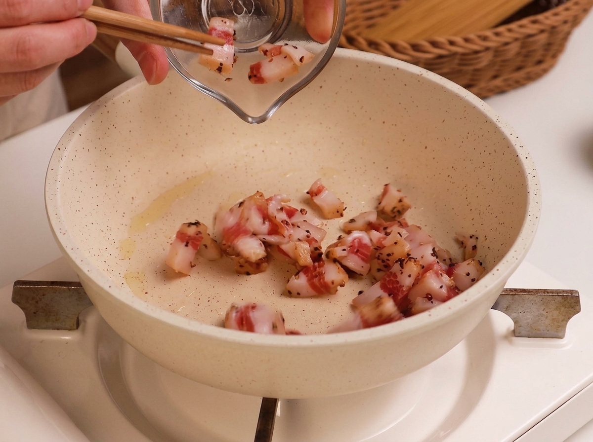 Gewürfeltes rohes Guanciale wird aus einer Glasschale in eine leicht geölte weiße Pfanne gegeben.
