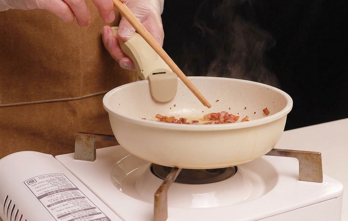 Guanciale-Würfel werden mit Stäbchen in einer Pfanne gerührt, während sie bräunen und Fett abgeben.