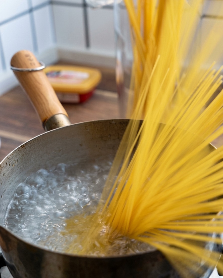 Eine Handvoll Spaghetti wird in einen Topf mit sprudelnd kochendem Wasser gegeben.