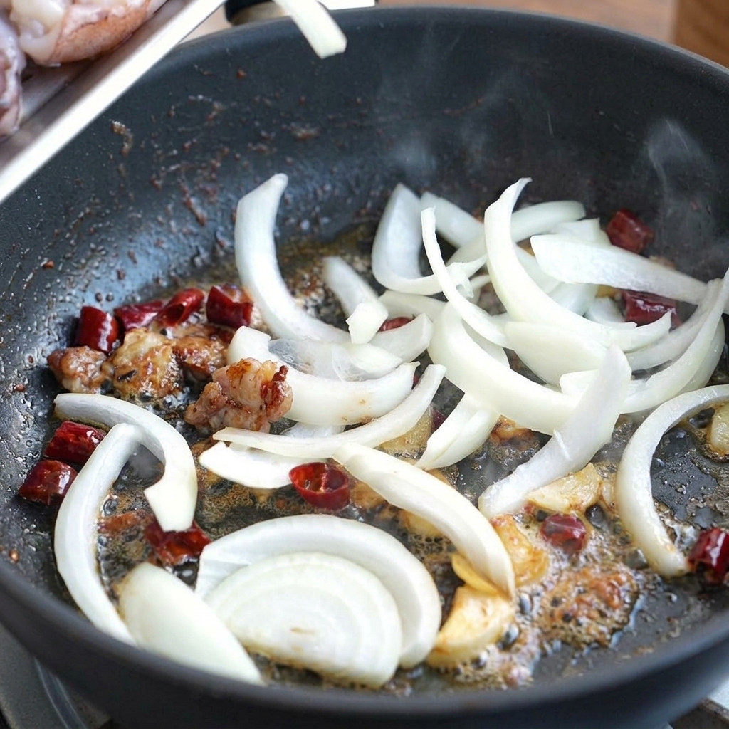 Weiße Zwiebelstreifen werden im aromatisierten Öl mit Chilis und Knoblauch geschwenkt.