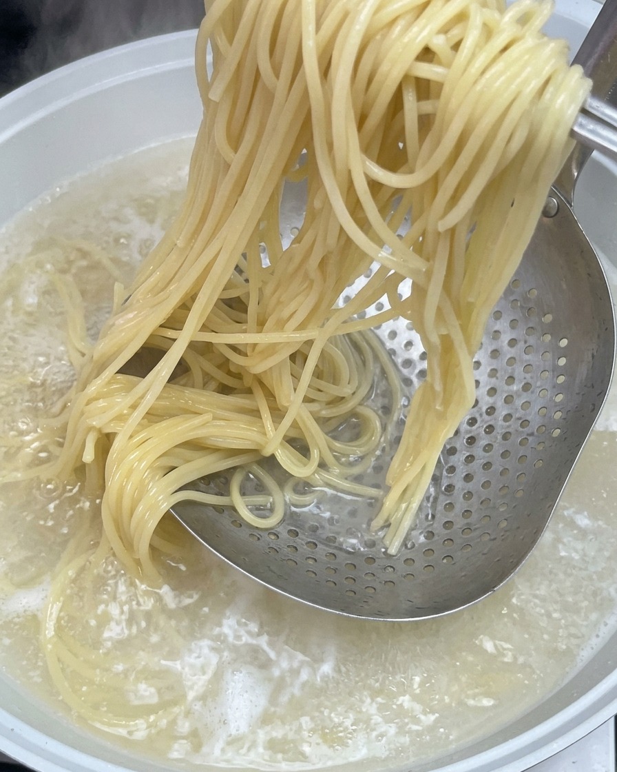 Gekochte Spaghetti werden mit einem Schaumlöffel aus dem heißen Wasser gehoben.