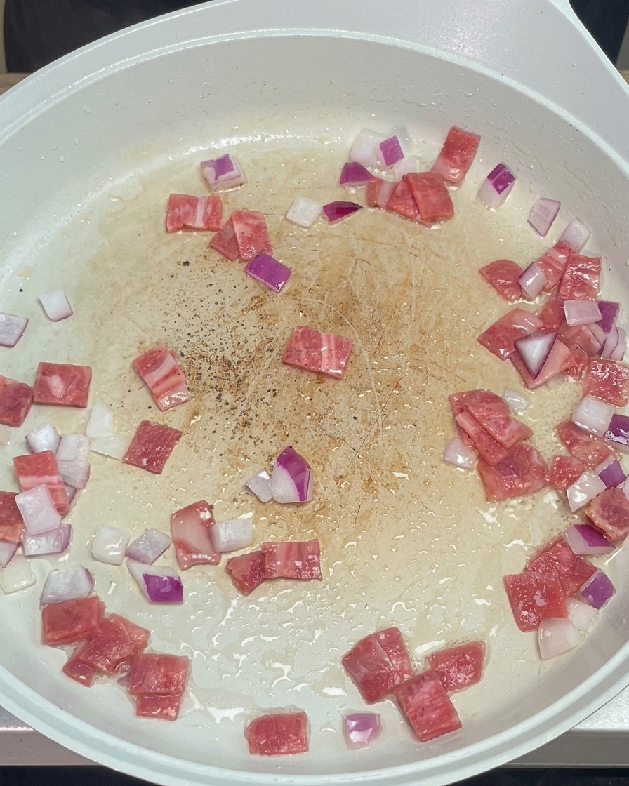 Gemahlener schwarzer Pfeffer wird über den Speck und die Zwiebeln in der Pfanne gestreut.