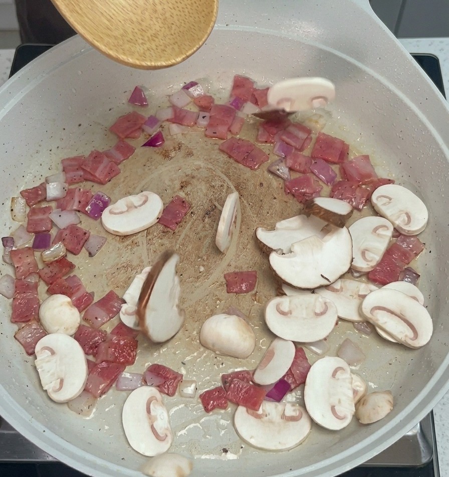 Geschnittene Champignons und Shiitake-Pilze werden zu Speck und Zwiebeln in die Pfanne gegeben.