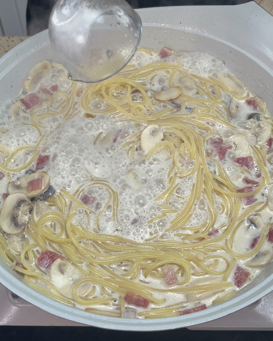 Ein Holzlöffel rührt die cremigen Spaghetti mit geschmolzenem Käse und Gewürzen um.
