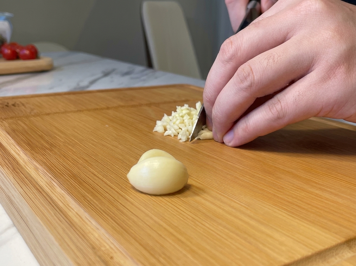 Feines Hacken von frischen Knoblauchzehen mit einem Messer auf einem Holzblock.