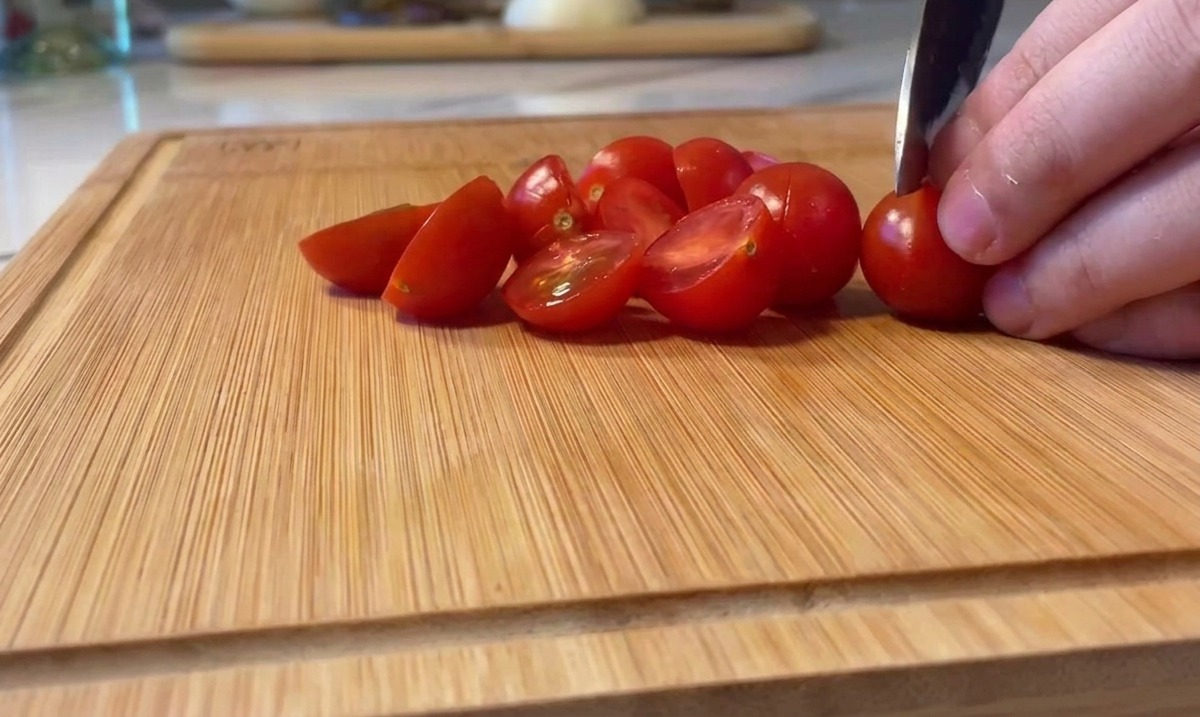 Leuchtend rote Kirschtomaten werden auf einem Holzschneidebrett halbiert.
