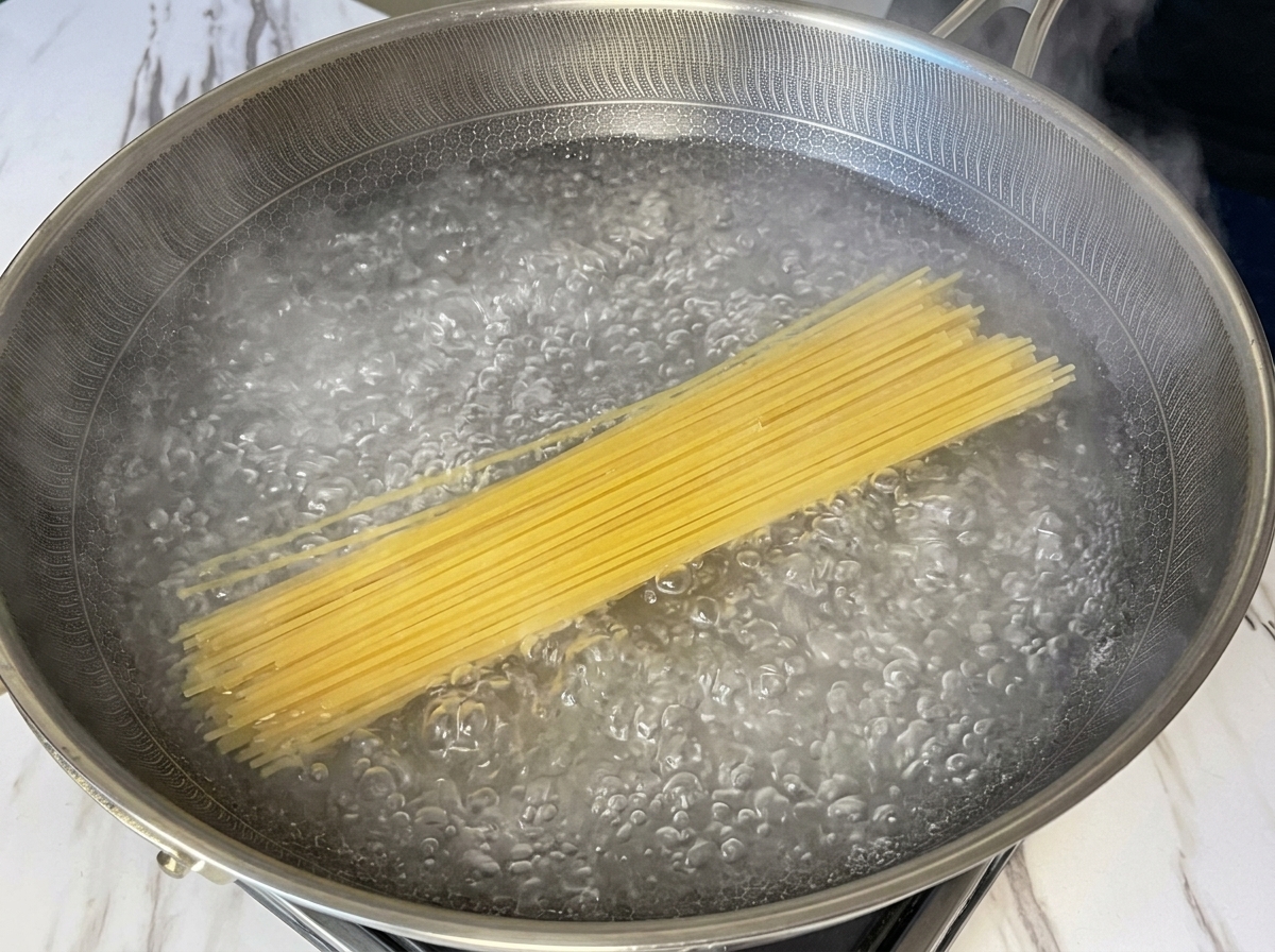 Trockene Spaghetti-Nudeln tauchen in einen breiten Topf mit sprudelnd kochendem Wasser ein.