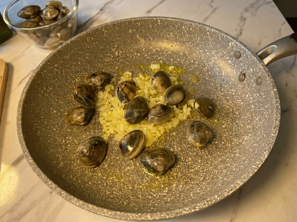 Frische, geschlossene Venusmuscheln werden in eine heiße Pfanne mit angeschwitztem Knoblauch und Zwiebeln gegeben.
