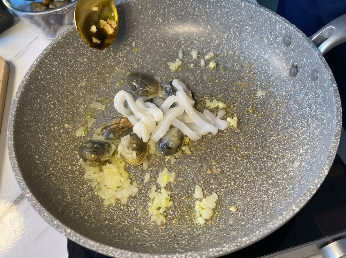 Rohe, weiße Tintenfischringe werden in eine heiße Pfanne mit Muscheln und Aromaten gegeben.