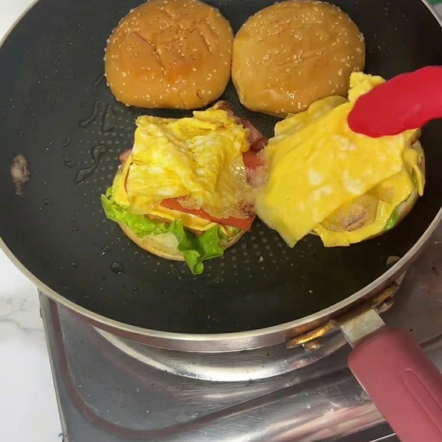 Ein fertiger Frühstücksburger auf einem Teller, die obere geröstete Sesam-Brötchenhälfte liegt fest auf.