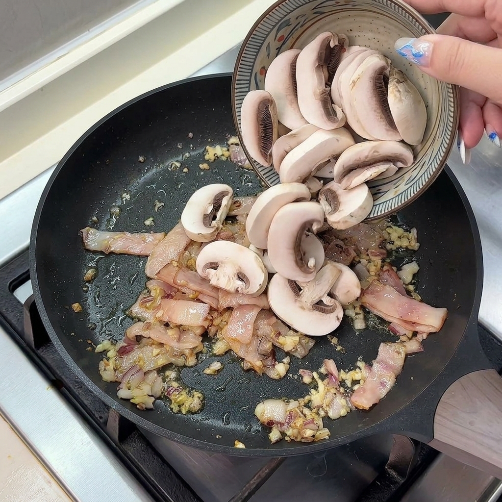 Frisch in Scheiben geschnittene Champignons werden aus einer Keramikschüssel in eine heiße Pfanne mit gebratenem Speck, Zwiebeln und Knoblauch gegeben.