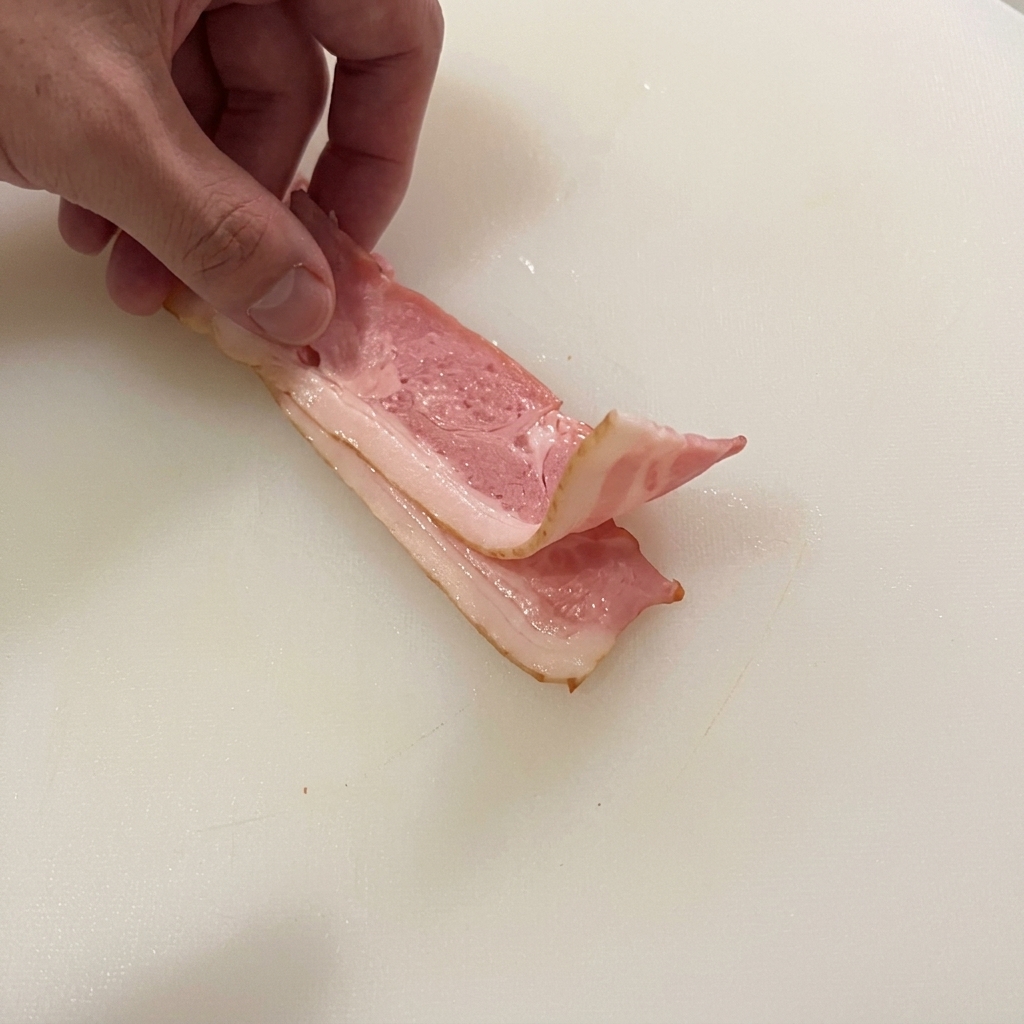 Rohe Speckstreifen werden auf einem weißen Brett in kleine Stücke geschnitten.