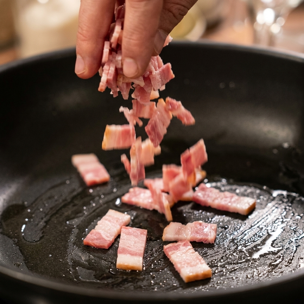 Gehackter Speck brät in einer dunklen Pfanne und lässt Fett aus.