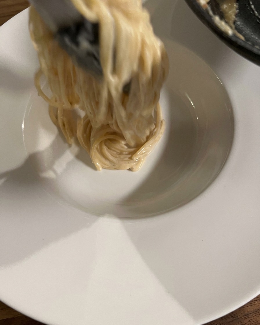 Eine Portion Carbonara wird mit der Zange elegant in einen tiefen Teller gedreht.
