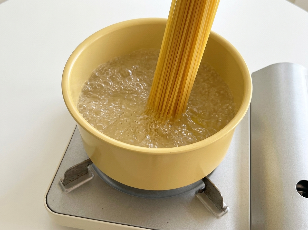 Trockene Spaghetti-Nudeln werden in einen gelben Topf mit kochendem Wasser gegeben.