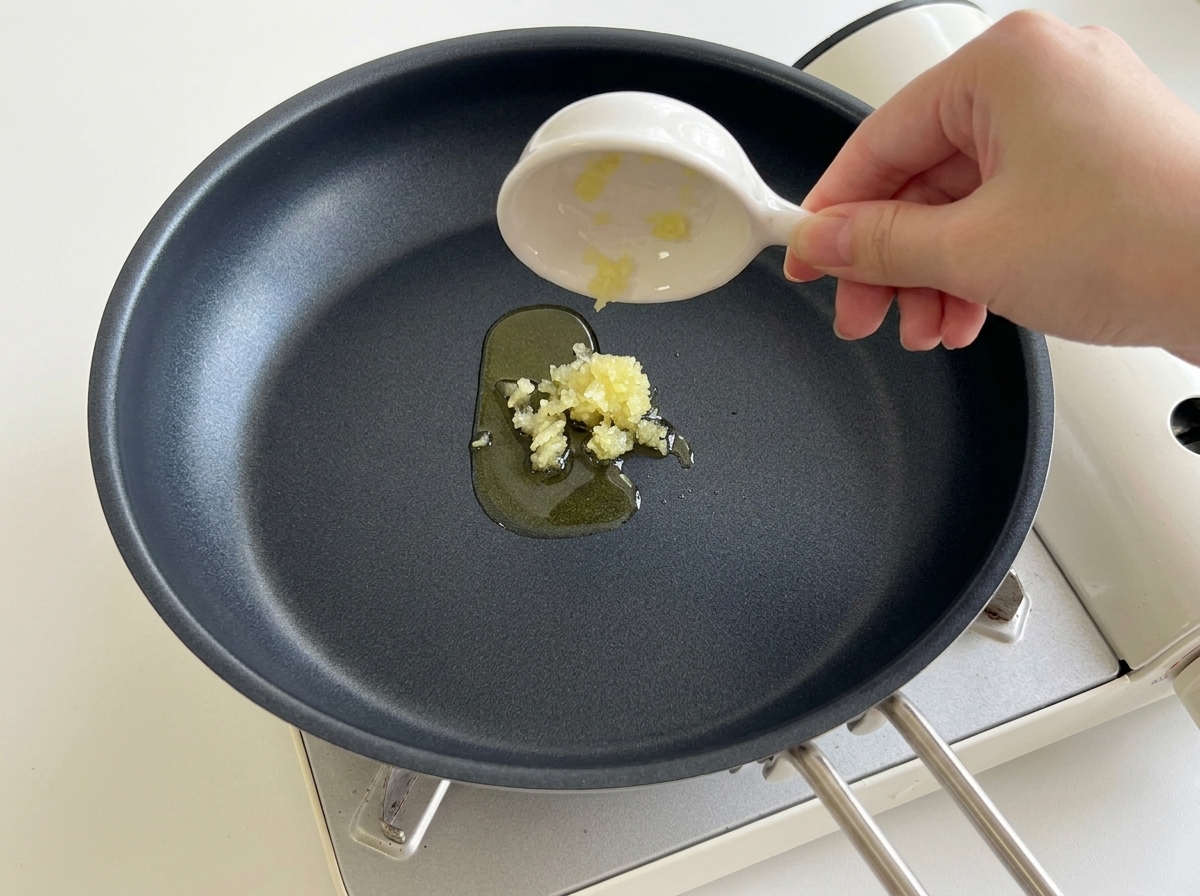 Gehackter Knoblauch wird aus einer kleinen Schale in eine erhitzte schwarze Pfanne mit Speiseöl gegeben.
