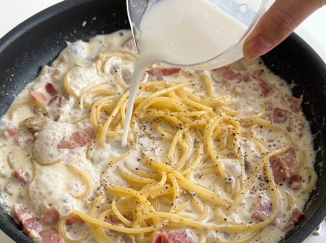 Eine weiße Stärkemischung wird über die Spaghetti in der cremigen Sauce gegossen.
