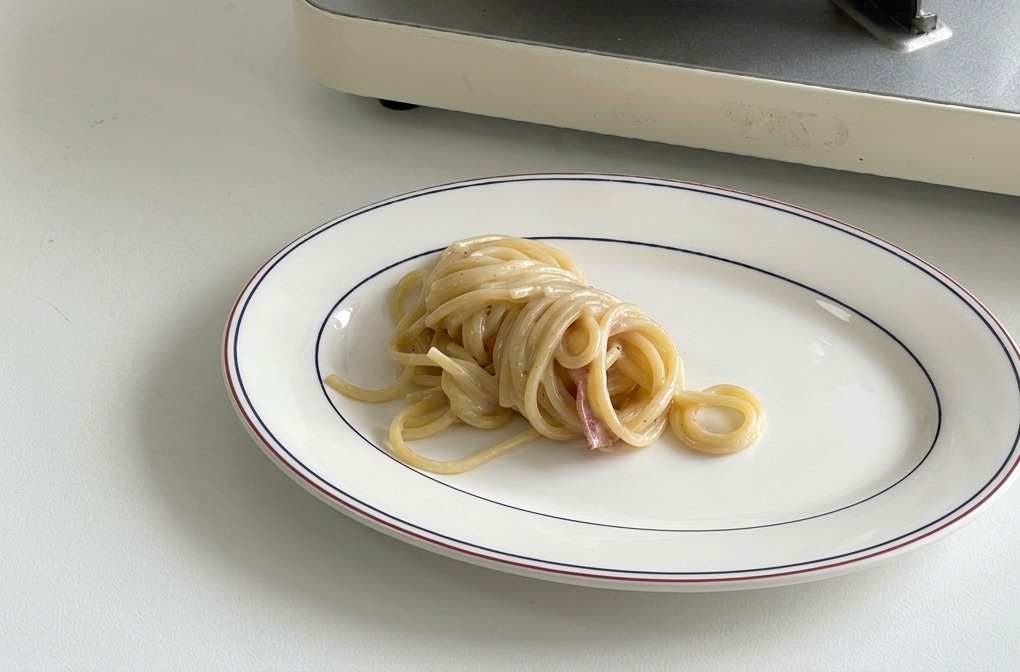 Ein ordentlich aufgedrehter Haufen cremiger Spaghetti in der Mitte eines weißen Tellers.