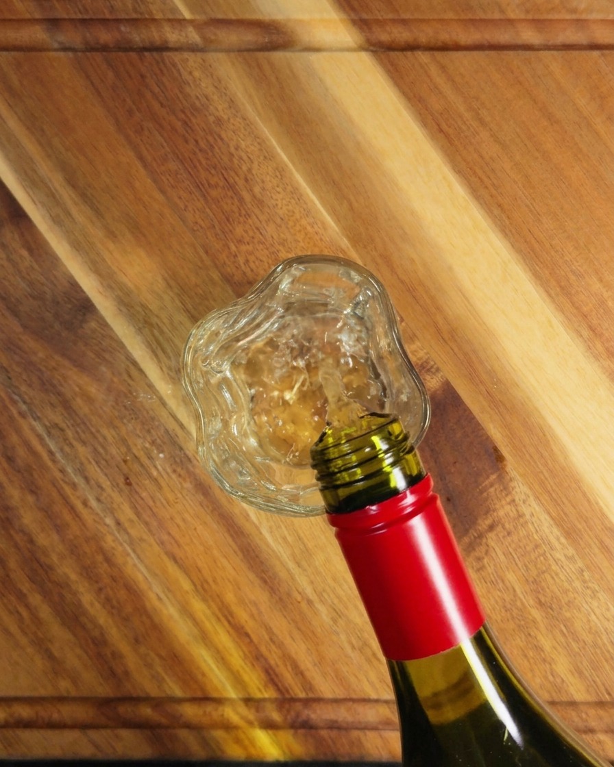 Weißwein wird aus einer grünen Flasche in ein kleines Glas auf einer Holzoberfläche gegossen.