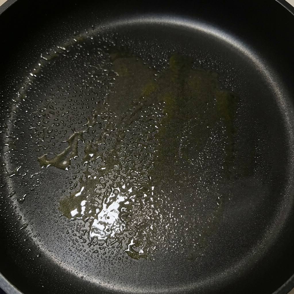 Eine schwarze Bratpfanne mit einer glänzenden Schicht aus geschmolzener Butter und Olivenöl.