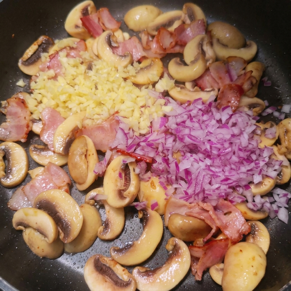 Frisch gehackte rote Zwiebeln und Knoblauch auf gebratenem Speck und Pilzen in einer Pfanne.