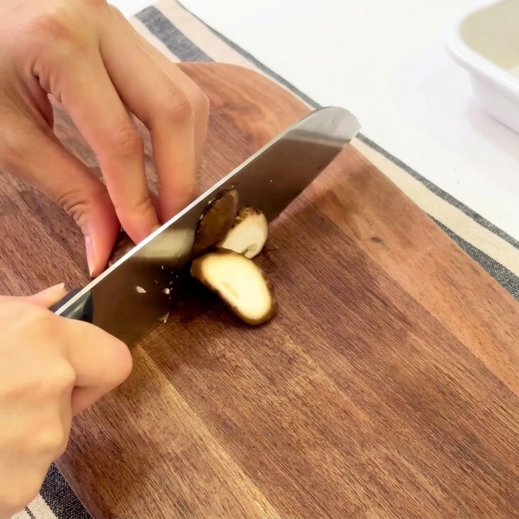 Hände schneiden frische Shiitake-Pilze auf einem Holzschneidebrett.