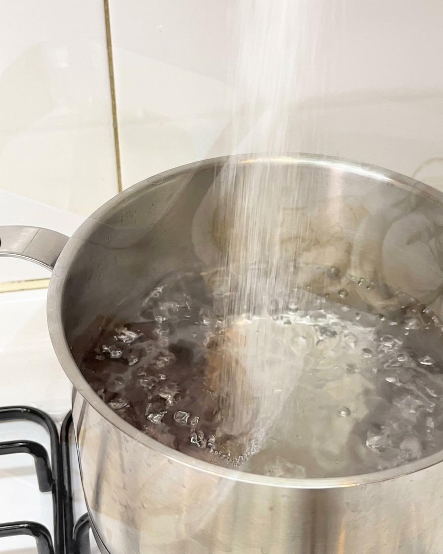 Salz wird in einen Edelstahltopf mit sprudelnd kochendem Wasser geschüttet.