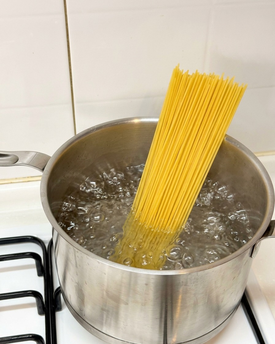Trockene Spaghetti werden in einen Topf mit kochendem Wasser auf dem Herd gegeben.