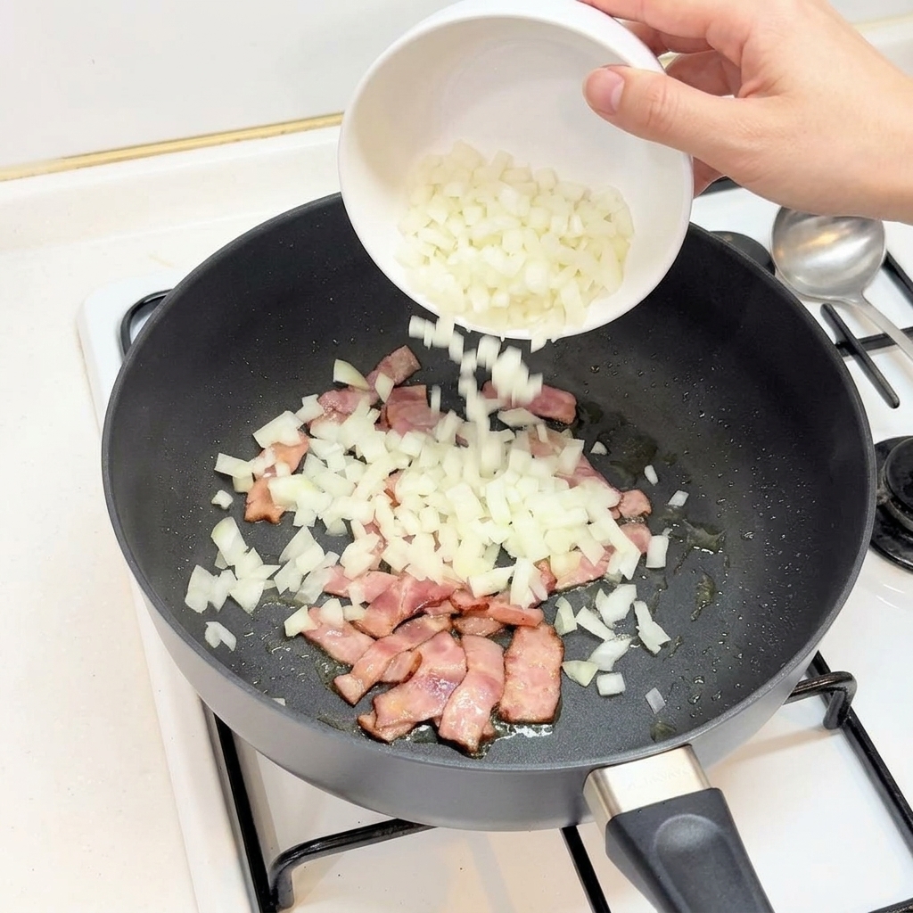Gehackte weiße Zwiebeln werden aus einer Schale zu dem gebratenen Speck in die Pfanne gegeben.