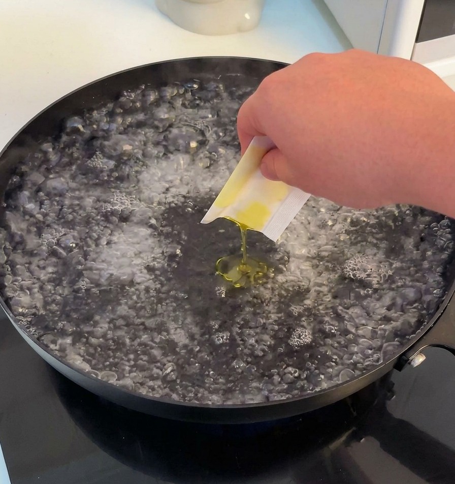 Eine Hand gibt Salz und etwas Olivenöl in einen großen Topf mit sprudelnd kochendem Wasser.