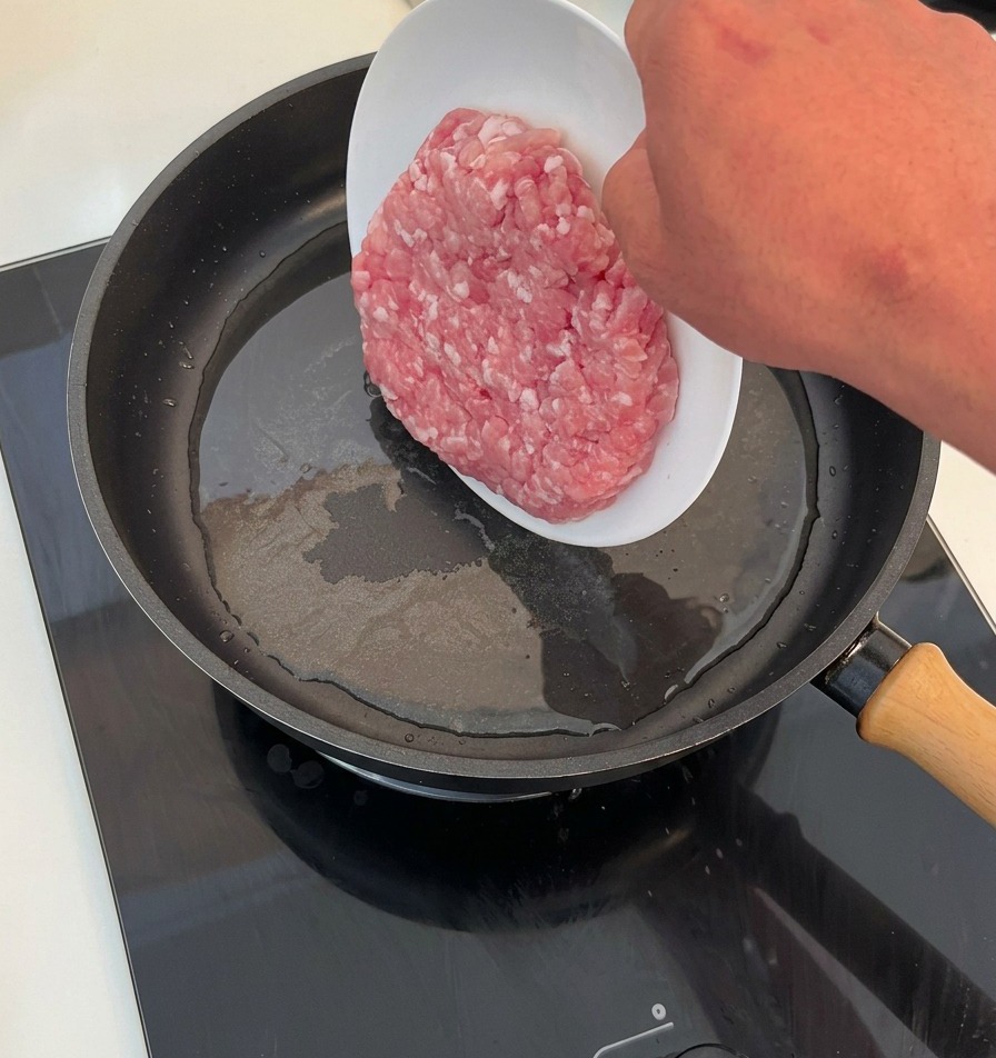 Rohes Hackfleisch wird von einem weißen Teller in eine heiße, geölte Pfanne gegeben.