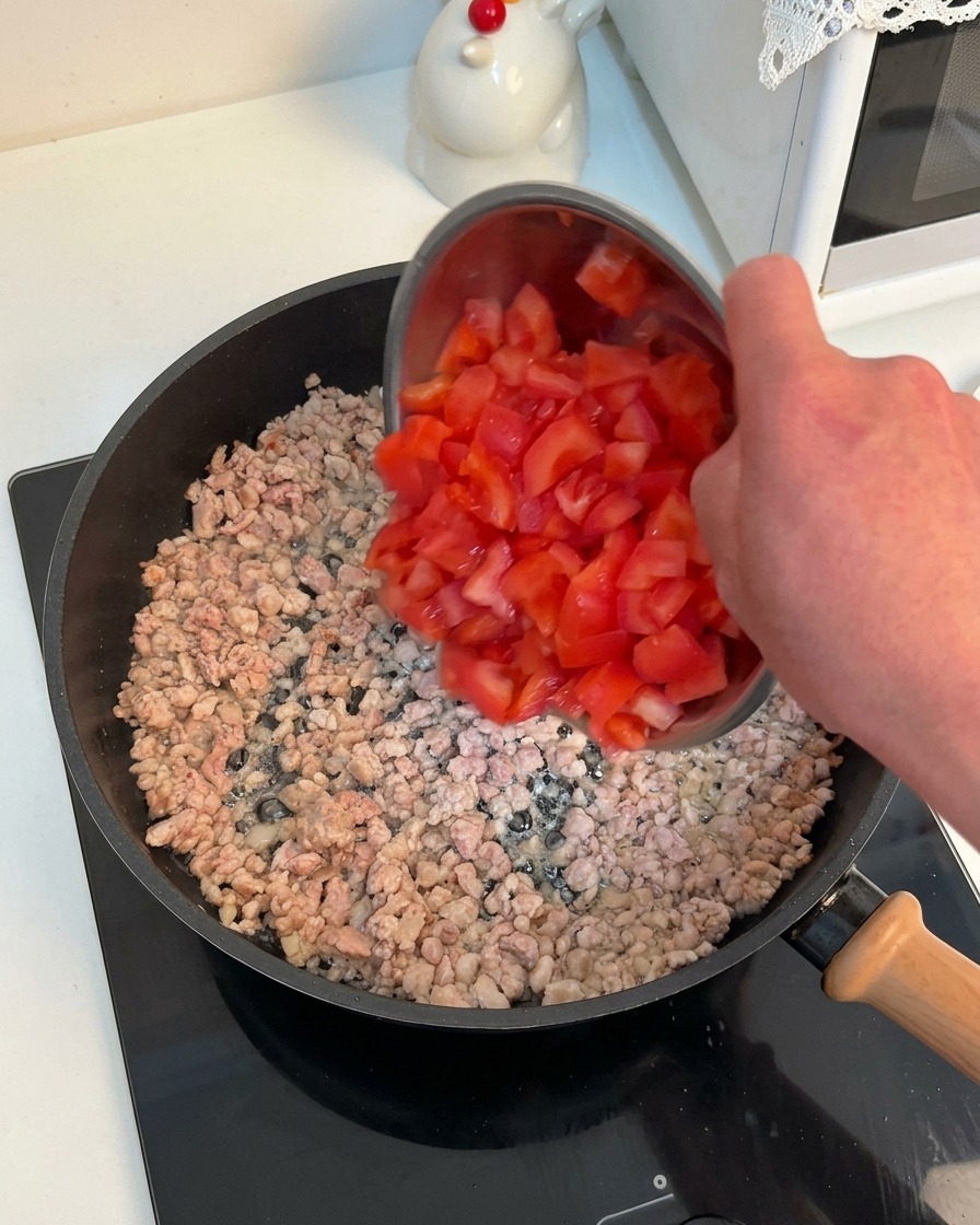 Leuchtend rote Tomatenwürfel werden in die heiße Pfanne mit dem angebratenen Hackfleisch geschüttet.
