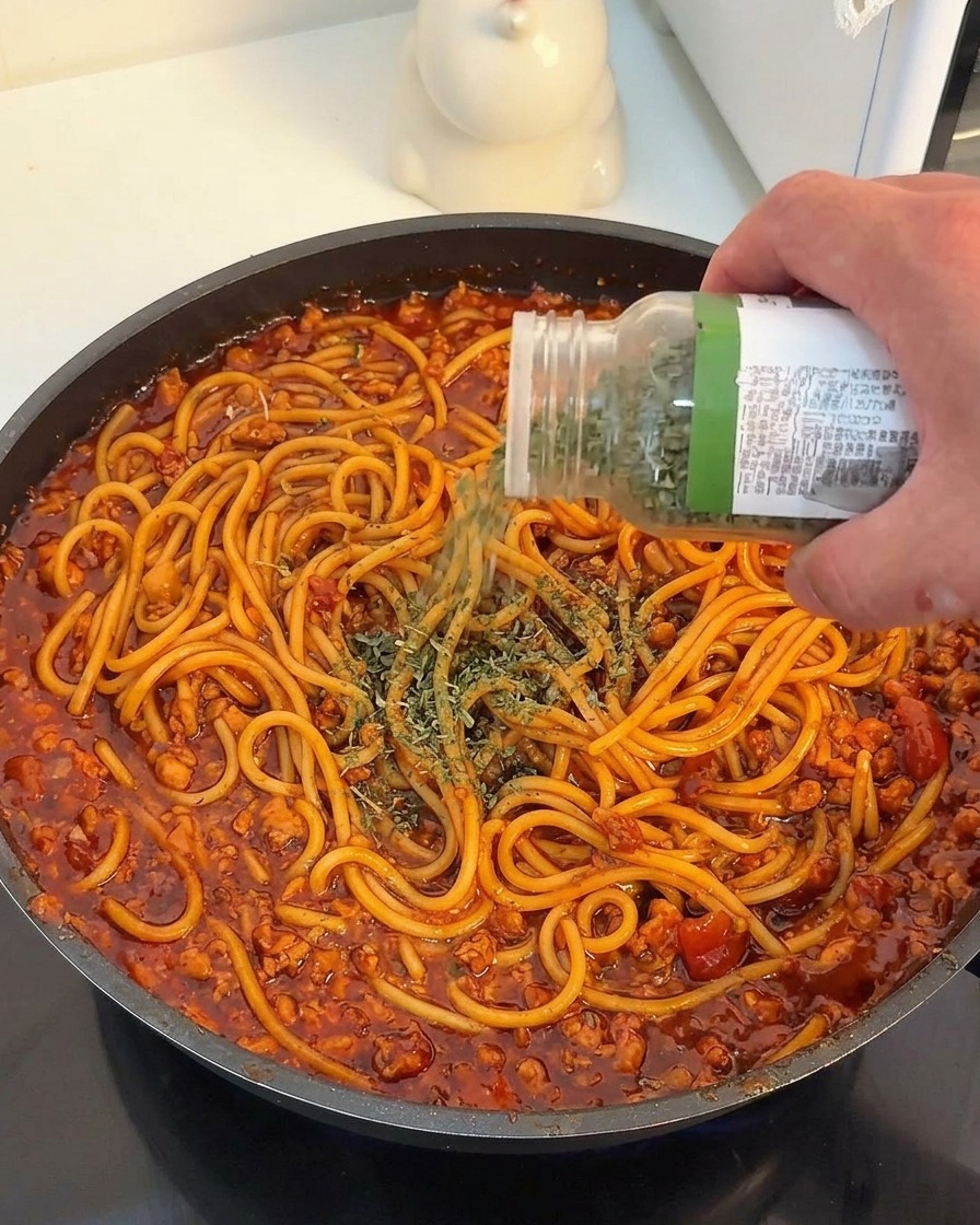 Getrocknete Petersilie wird über die fertig gemischten Spaghetti mit roter Soße gestreut.