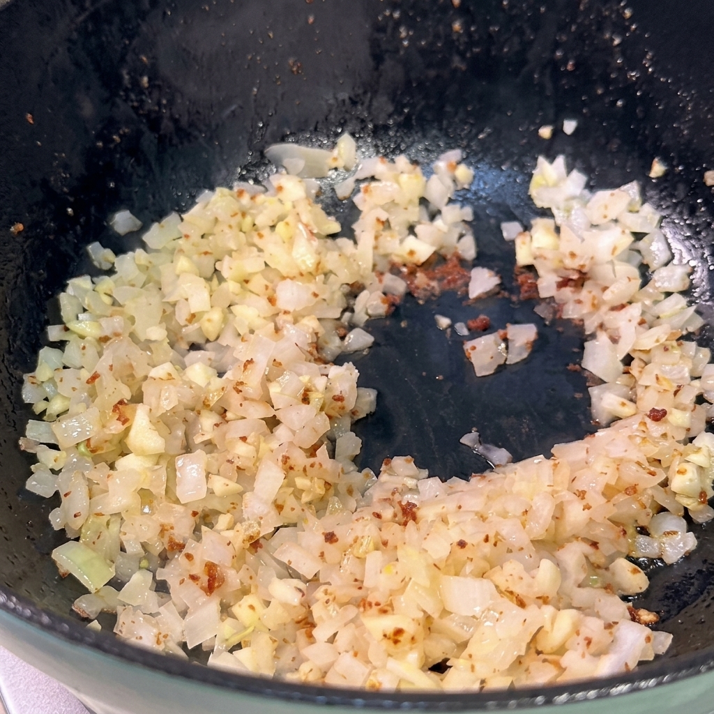 Gehackte Zwiebeln und Knoblauch werden in einer dunklen Pfanne gedünstet und werden langsam glasig.