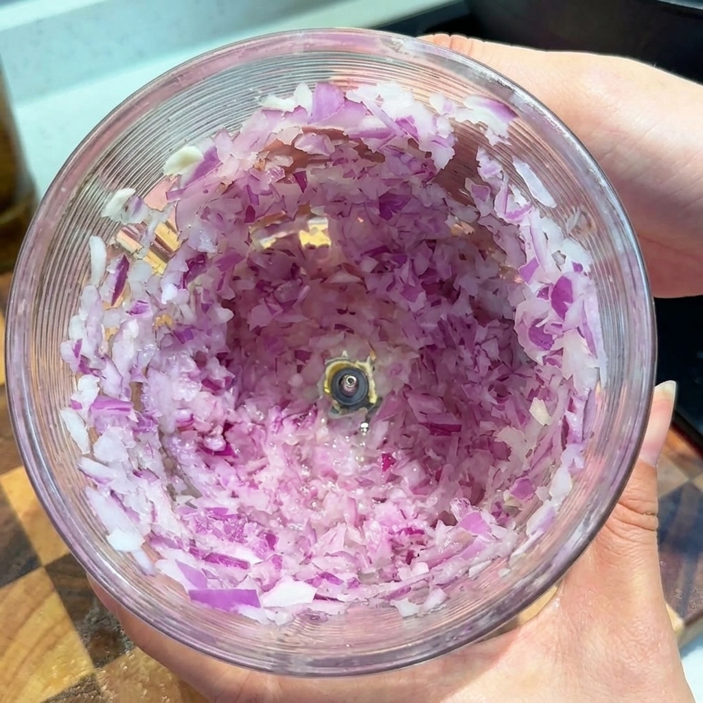 Fein gehackte rote Zwiebeln in einem transparenten Behälter einer Küchenmaschine.