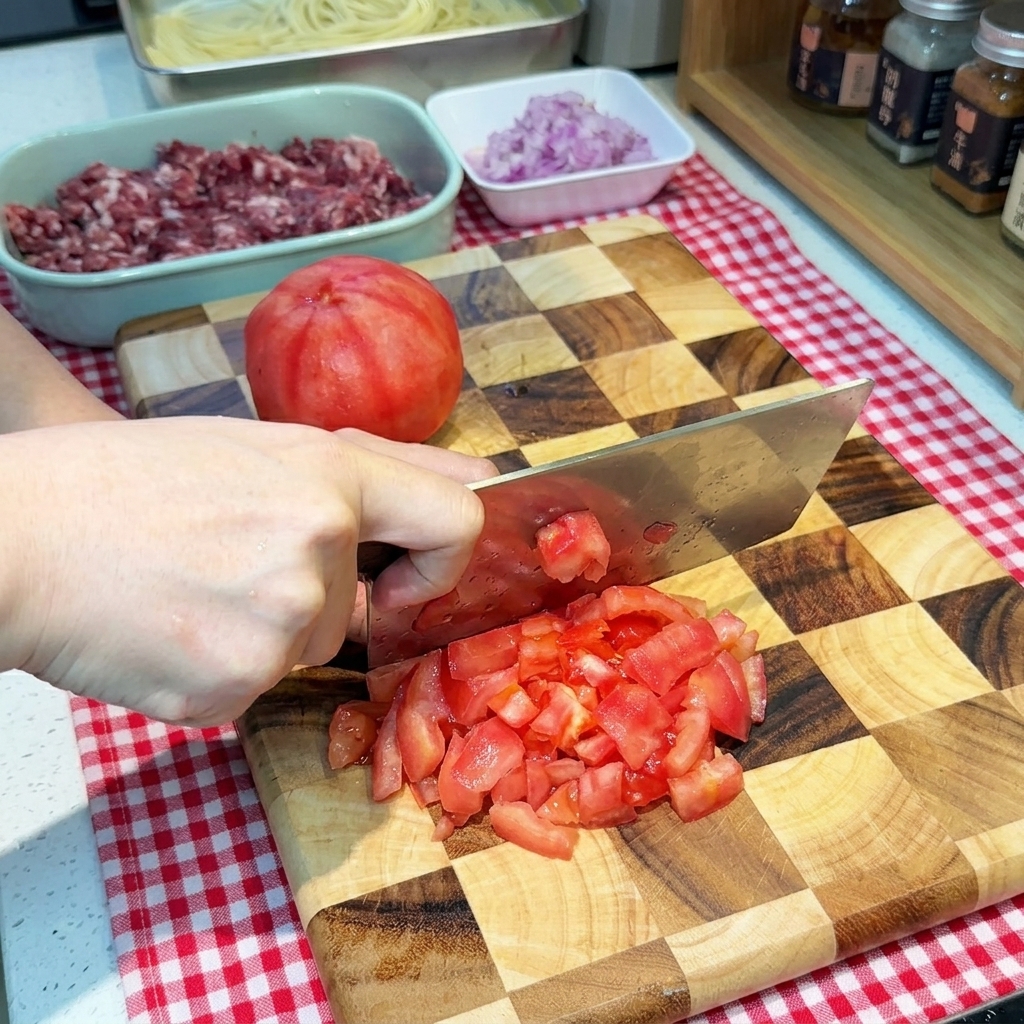 Eine Hand schneidet eine geschälte rote Tomate mit einem breiten Messer in kleine Würfel auf einem Schneidebrett.