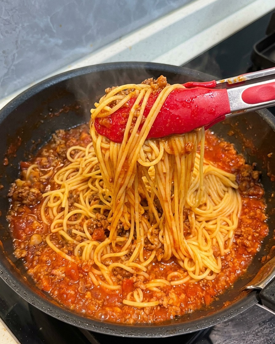 Rote Küchenzangen heben Spaghetti an, die rundum mit einer dicken, herzhaften Fleischsauce überzogen sind.