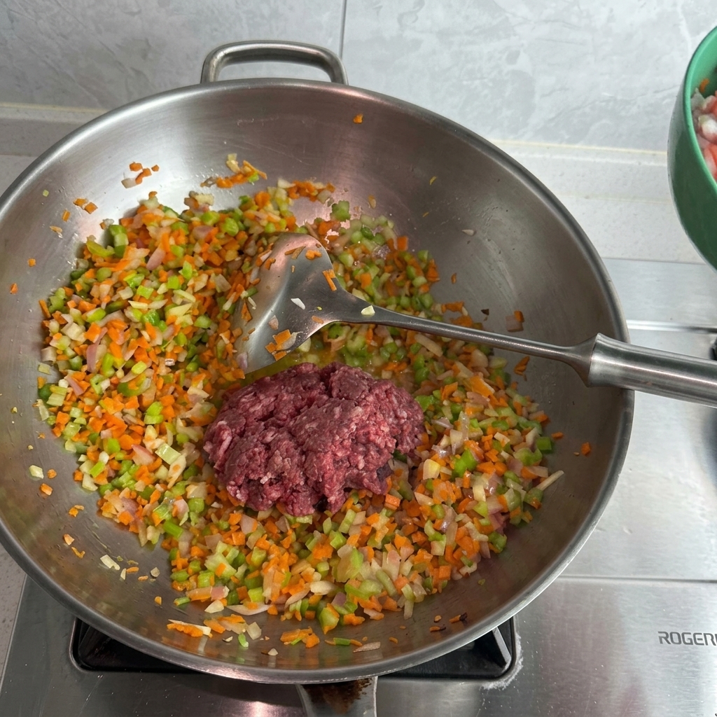 Eine Mischung aus rohem Schweine- und Rinderhackfleisch liegt auf dem gedünsteten Gemüse im Wok.