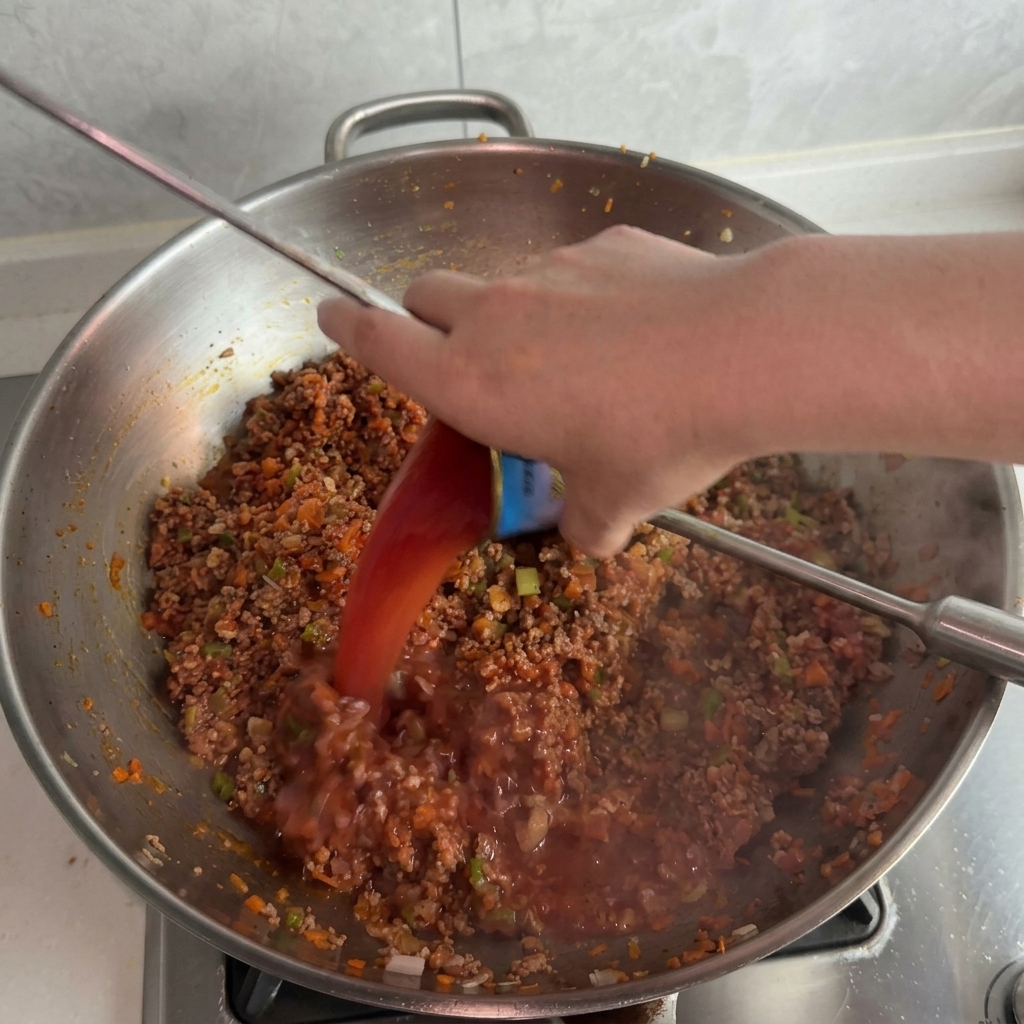 Wasser wird aus einer Dose in die blubbernde Fleischsauce gegossen.