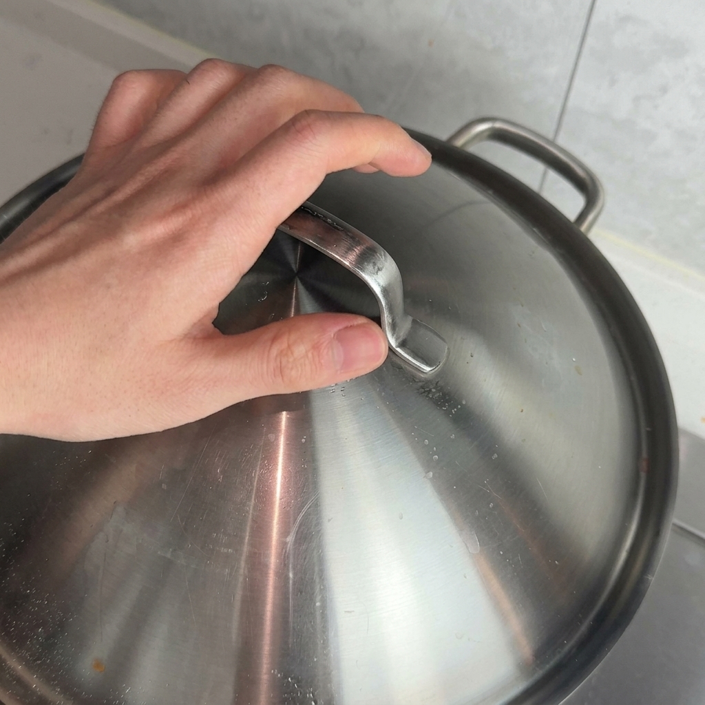 Ein Metalldeckel wird auf den Topf gesetzt, um die Sauce schmoren zu lassen.