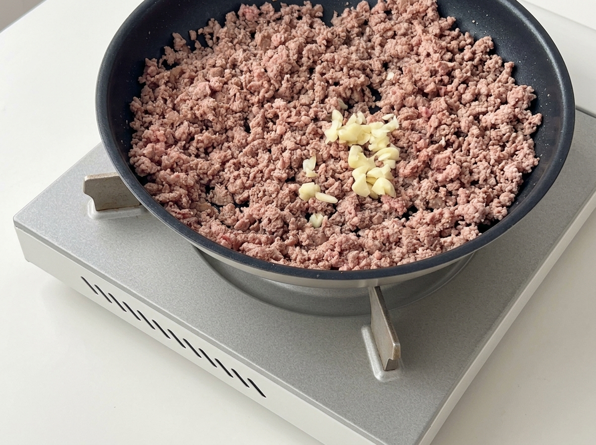 Gehackter Knoblauch wird auf das gebräunte Fleisch in der Pfanne gegeben.