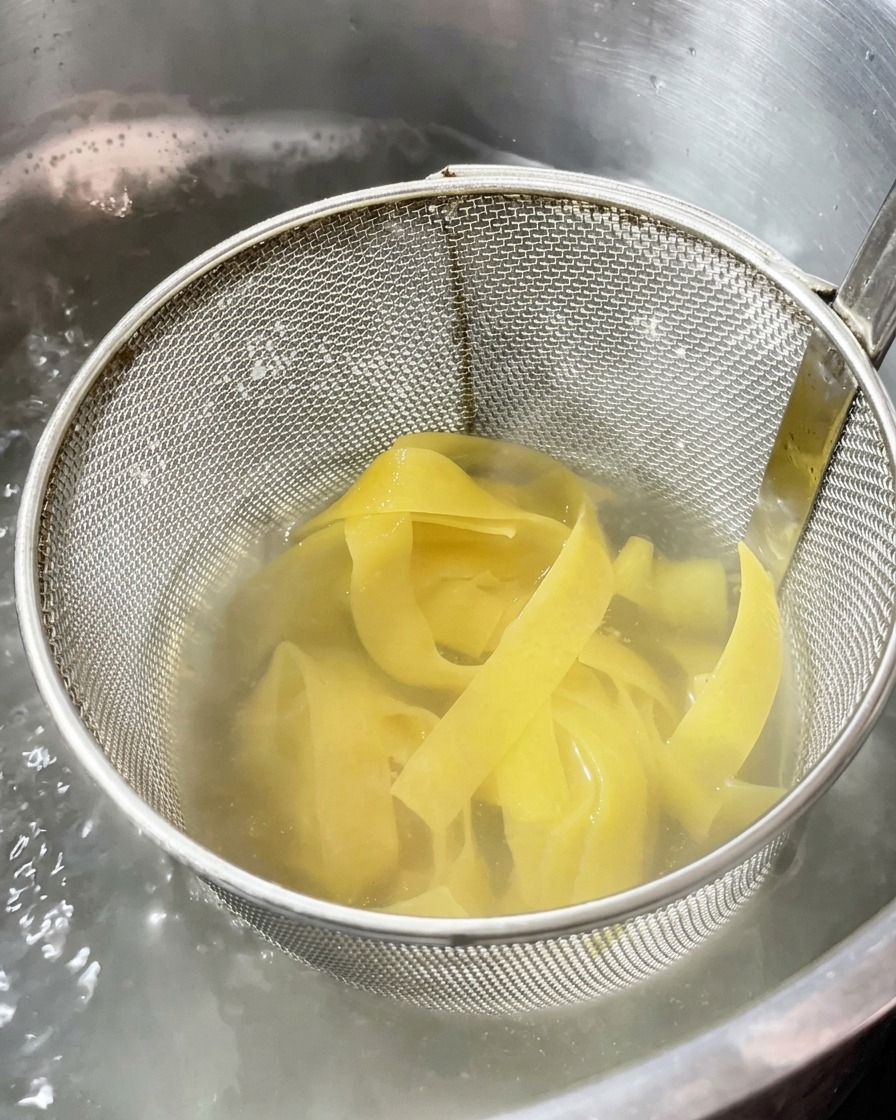 Breite Bandnudeln kochen in einem Metallsieb in einem Topf mit kochendem Wasser.