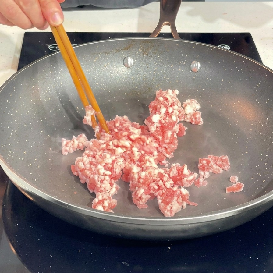 Verwendung von Stäbchen, um rohes Schweinehackfleisch in einer heißen Pfanne zu zerkleinern.