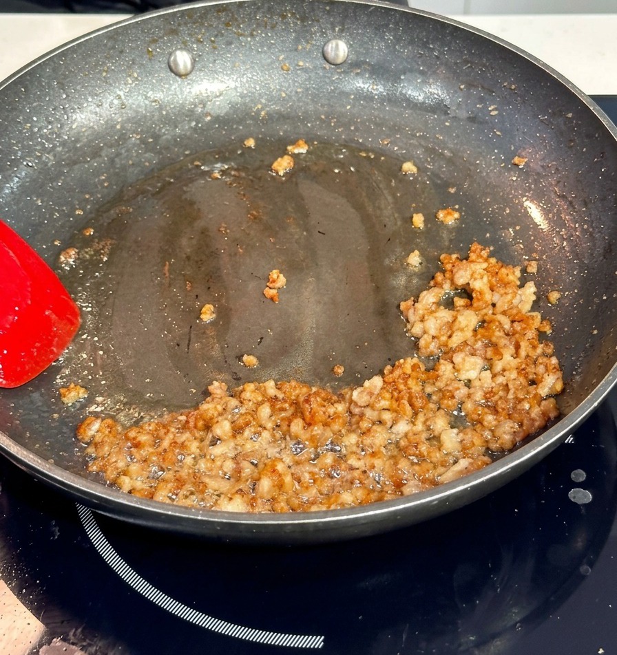 Anbräunen von Schweinehackfleisch in einer dunklen Antihaftpfanne mit einem roten Pfannenwender.