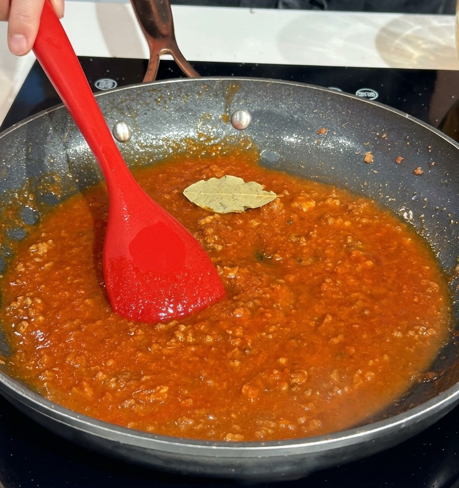 Ein getrocknetes Lorbeerblatt liegt auf der kräftig roten Fleischsauce in der Pfanne.