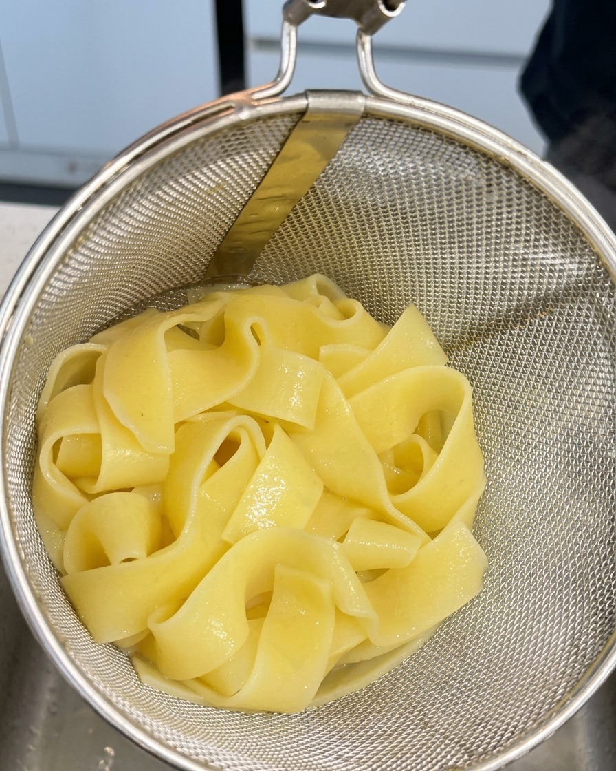 Gekochte Pappardelle ruhen in einem Metallsieb nach dem Herausnehmen aus dem Wasser.