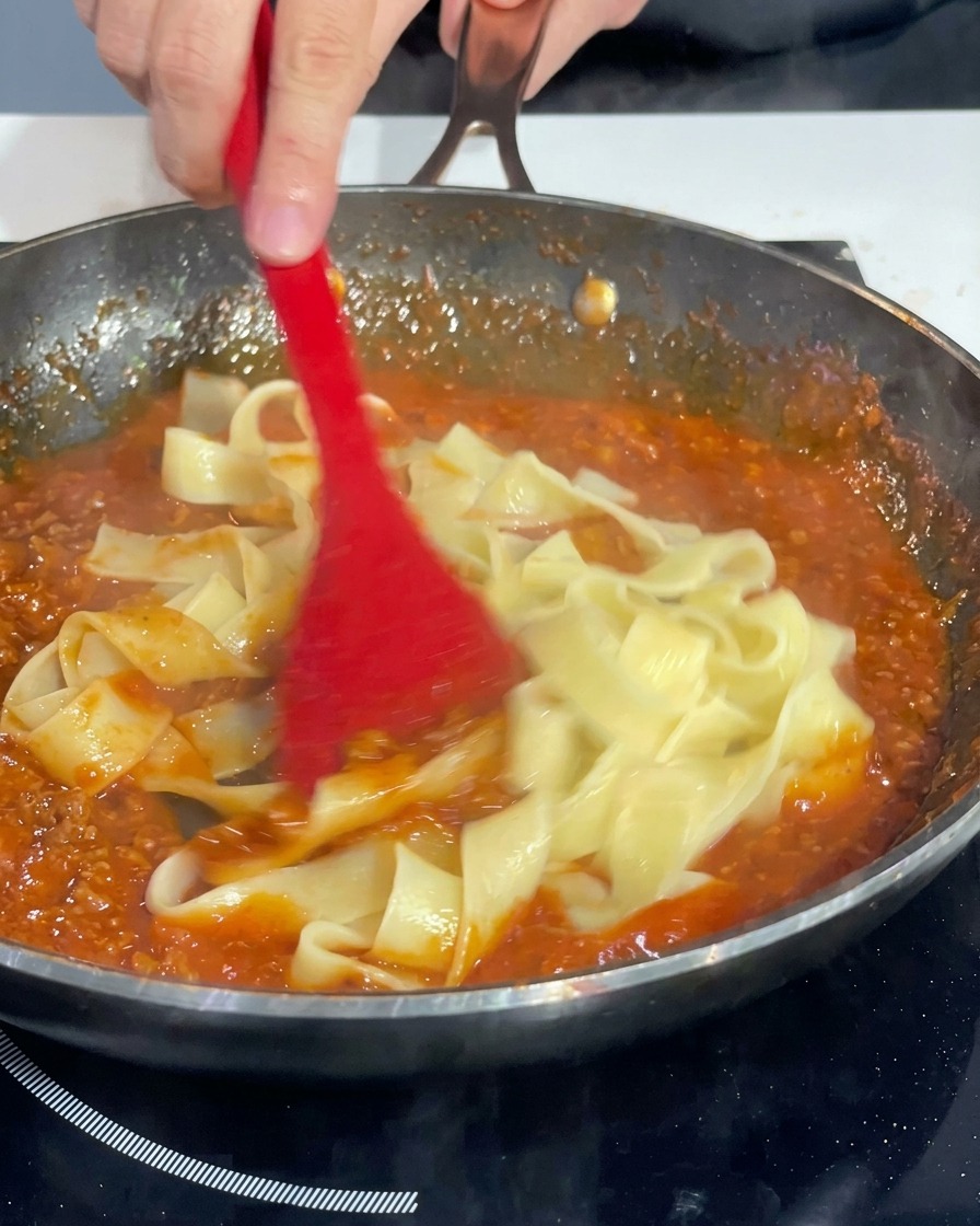 Pappardelle werden in der Pfanne gewendet und gleichmäßig mit der dicken Bolognese überzogen.