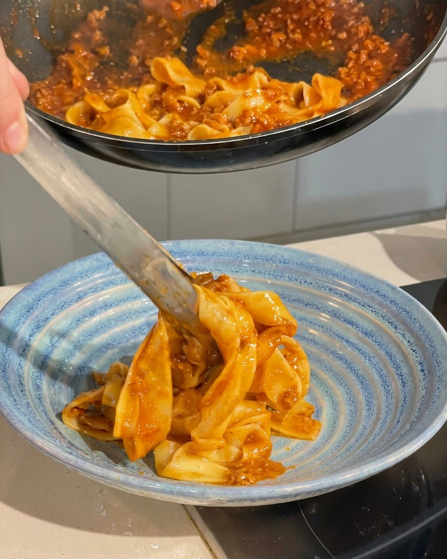 Servieren der Pasta mit einer Küchenzange in eine tiefblaue Keramikschüssel.